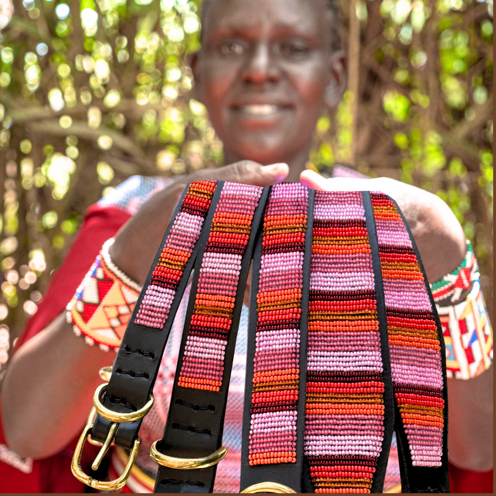 Maasai woman showcasing her handmade beaded leather dog collars and leashes for The Maasai Collection featuring the pink and gold Flamingo design on black leather