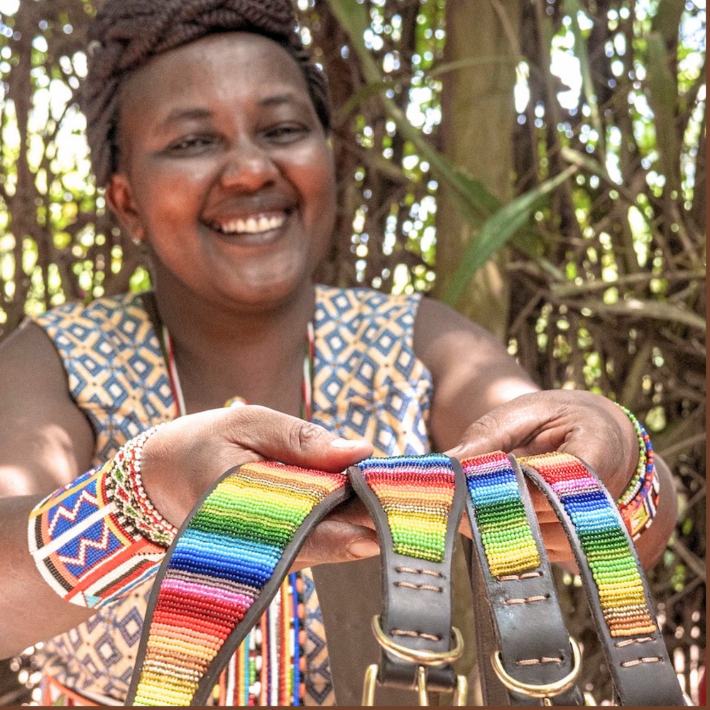 Maasai Mara Mama in traditional clothing showcasing her hand made dog collars in a Rainbow design for The Maasai Collection