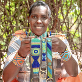 Maasai woman in traditional clothing showcasing her handmade dog collars for The Maasai Collection featuring the blue green and gold Peacock design