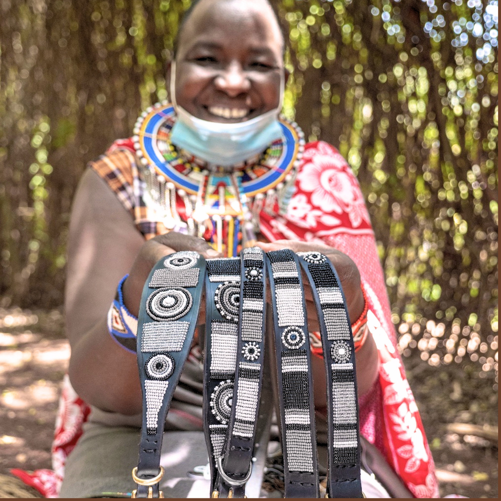 Maasai Mara Mama in traditional clothing showcasing her hand made dog collars and leashes for The Maasai Collection featuring the black white and silver Moonlight design on black leather
