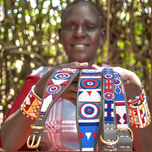 Maasai Mara Mama in traditional clothing showcasing her handmade artisan dog collars for The Maasai Collection in the red white and blue Liberty design 