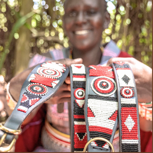 Maasai woman in traditional clothing showcasing her hand made dog collars and leashes for The Maasai Collection featuring the black white and red Pride design on black leather