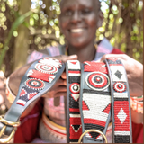 Maasai woman in traditional clothing showcasing her hand made dog collars and leashes for The Maasai Collection featuring the black white and red Pride design on black leather