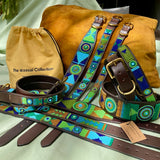 group photo of multiple different sizes and widths of blue green and gold handmade beaded leather collars on dark brown leather from The Maasai Collection in their Peacock design